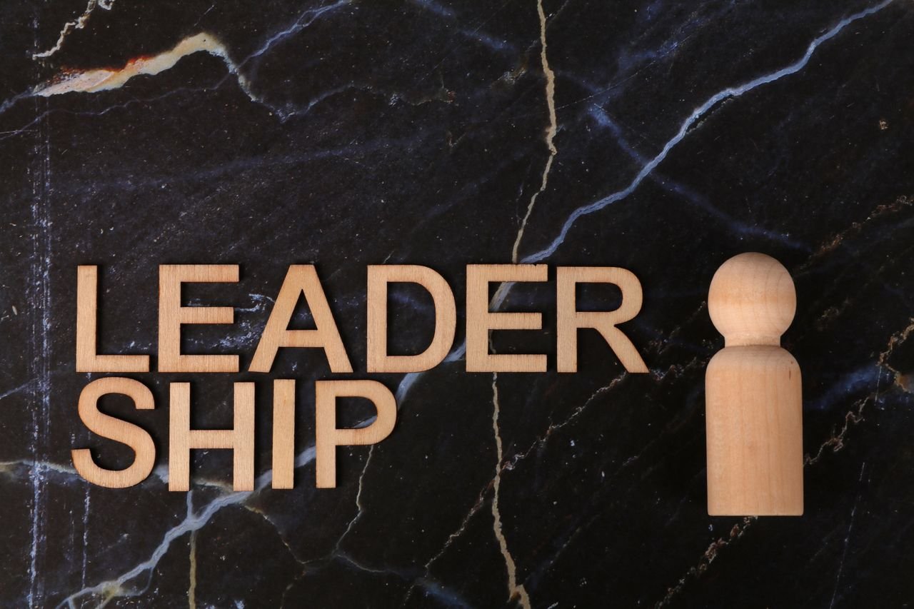 Wooden leadership text and figurine on marble representing management concepts.